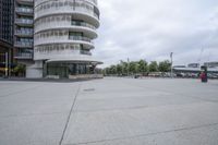 a empty parking lot next to tall buildings with cars in front of it and trees in the background