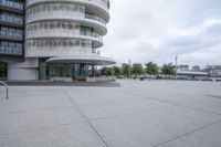 a empty parking lot next to tall buildings with cars in front of it and trees in the background