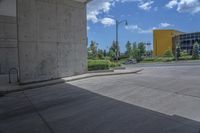 an empty cement parking lot with many bushes and buildings on the horizon in the background