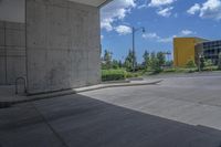 an empty cement parking lot with many bushes and buildings on the horizon in the background