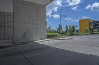 an empty cement parking lot with many bushes and buildings on the horizon in the background