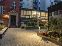 an exterior shot of two buildings at night, with lots of plants in the courtyard