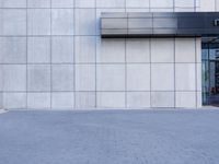 a gray concrete building with metal cladding and doors, sitting on a brick sidewalk