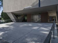 a building with a bench outside on concrete surface with walkway underneath a roof and trees