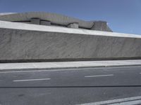 an empty city sidewalk next to a cement building with a sloped roof and curve - like edge