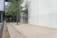 a concrete building with glass windows and a planter below it on the sidewalk by some trees