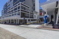 a tall white building near a street with many cars and pedestrians on a sidewalk outside of it