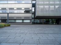 a person rides their skate board in a courtyard area with grey stone floors and many windows