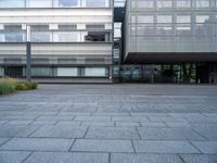 a person rides their skate board in a courtyard area with grey stone floors and many windows