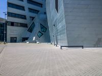 the large building has a large blue facade and a long grey bench in the front