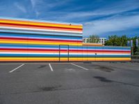 an empty parking lot painted brightly stripes on the wall of the building and sky as well as stones