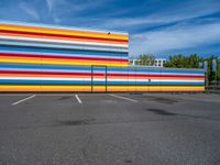 an empty parking lot painted brightly stripes on the wall of the building and sky as well as stones