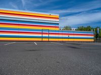 an empty parking lot painted brightly stripes on the wall of the building and sky as well as stones