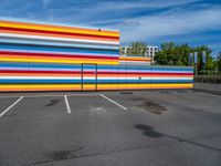 an empty parking lot painted brightly stripes on the wall of the building and sky as well as stones