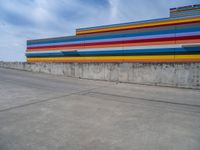 an empty parking lot painted brightly stripes on the wall of the building and sky as well as stones