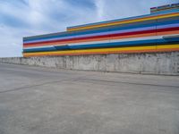 an empty parking lot painted brightly stripes on the wall of the building and sky as well as stones