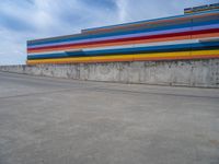 an empty parking lot painted brightly stripes on the wall of the building and sky as well as stones