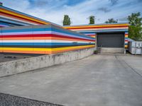 an empty parking lot painted brightly stripes on the wall of the building and sky as well as stones