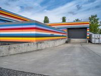 an empty parking lot painted brightly stripes on the wall of the building and sky as well as stones