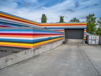 an empty parking lot painted brightly stripes on the wall of the building and sky as well as stones