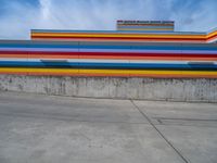 an empty parking lot painted brightly stripes on the wall of the building and sky as well as stones