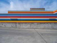 an empty parking lot painted brightly stripes on the wall of the building and sky as well as stones