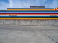 an empty parking lot painted brightly stripes on the wall of the building and sky as well as stones