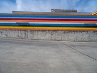 an empty parking lot painted brightly stripes on the wall of the building and sky as well as stones