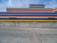 an empty parking lot painted brightly stripes on the wall of the building and sky as well as stones