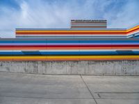 an empty parking lot painted brightly stripes on the wall of the building and sky as well as stones