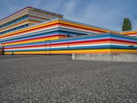 an empty parking lot painted brightly stripes on the wall of the building and sky as well as stones