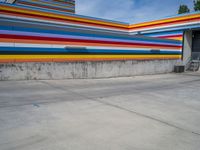 an empty parking lot painted brightly stripes on the wall of the building and sky as well as stones