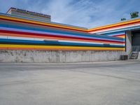 an empty parking lot painted brightly stripes on the wall of the building and sky as well as stones