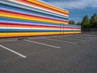 an empty parking lot painted brightly stripes on the wall of the building and sky as well as stones