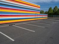 an empty parking lot painted brightly stripes on the wall of the building and sky as well as stones