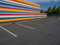 an empty parking lot painted brightly stripes on the wall of the building and sky as well as stones