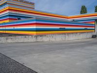 an empty parking lot painted brightly stripes on the wall of the building and sky as well as stones