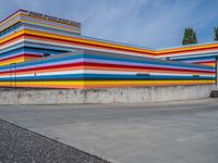 an empty parking lot painted brightly stripes on the wall of the building and sky as well as stones