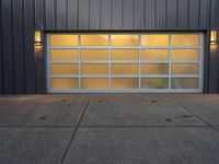 a modern garage door on a concrete sidewalk in front of a gray metal building at dusk