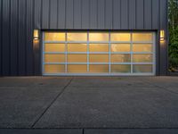 a modern garage door on a concrete sidewalk in front of a gray metal building at dusk