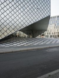 a very wide glass building in the middle of the road with another building near by
