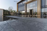 large glass window building next to water pool with reflection in window above concrete flooring