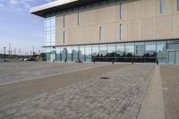 a glass building has benches on the sidewalk in front of it and cars parked in the driveway nearby