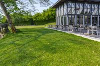 large patio in front of glass covered building with lawn area between it and trees outside