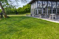 large patio in front of glass covered building with lawn area between it and trees outside