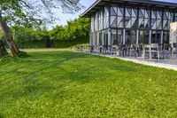 large patio in front of glass covered building with lawn area between it and trees outside