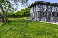 large patio in front of glass covered building with lawn area between it and trees outside