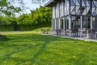 large patio in front of glass covered building with lawn area between it and trees outside