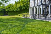 large patio in front of glass covered building with lawn area between it and trees outside