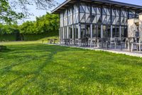 large patio in front of glass covered building with lawn area between it and trees outside